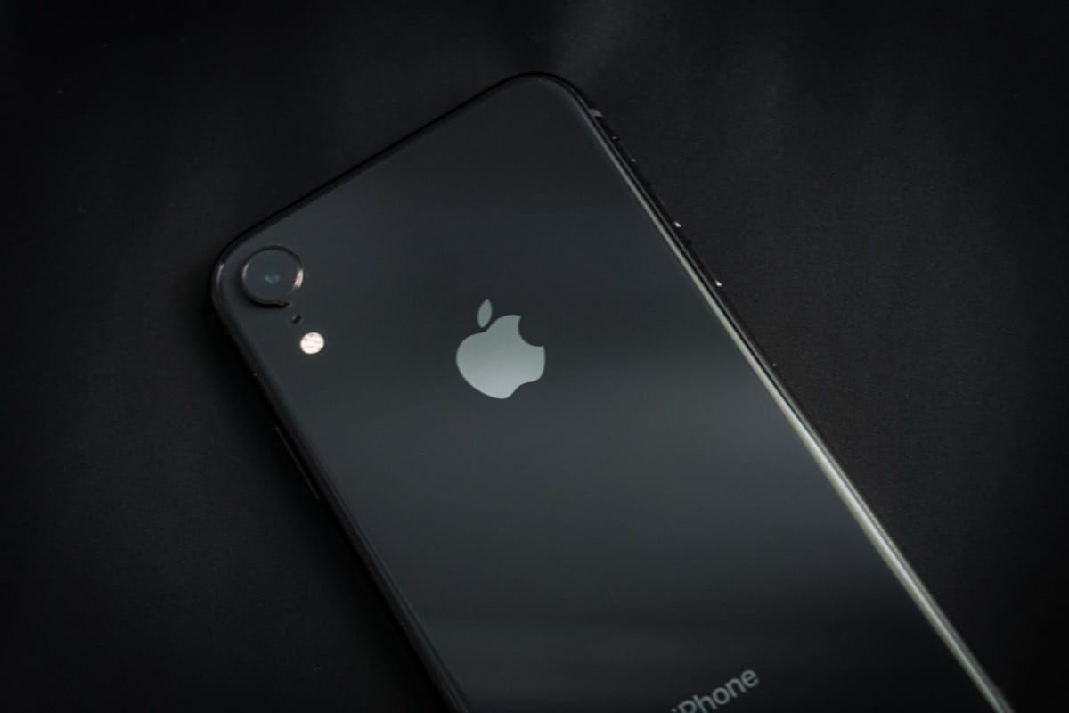 A black iPhone lying face down on a dark surface, showing the Apple logo and rear camera.