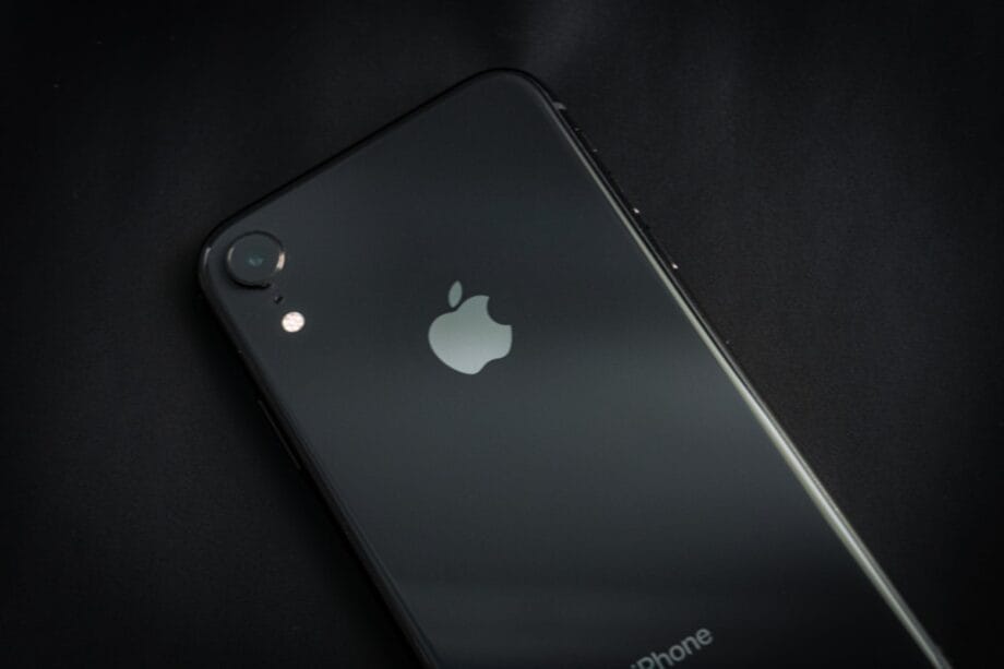 A black iPhone is placed face down on a dark surface, showing the Apple logo and rear camera.