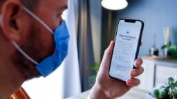 A person wearing a blue face mask looks at a smartphone displaying Face ID instructions in French.