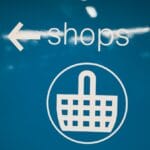 White text and icon on blue background showing an arrow pointing left, the word shops, and a shopping basket symbol.