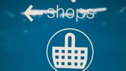White text and icon on blue background showing an arrow pointing left, the word shops, and a shopping basket symbol.