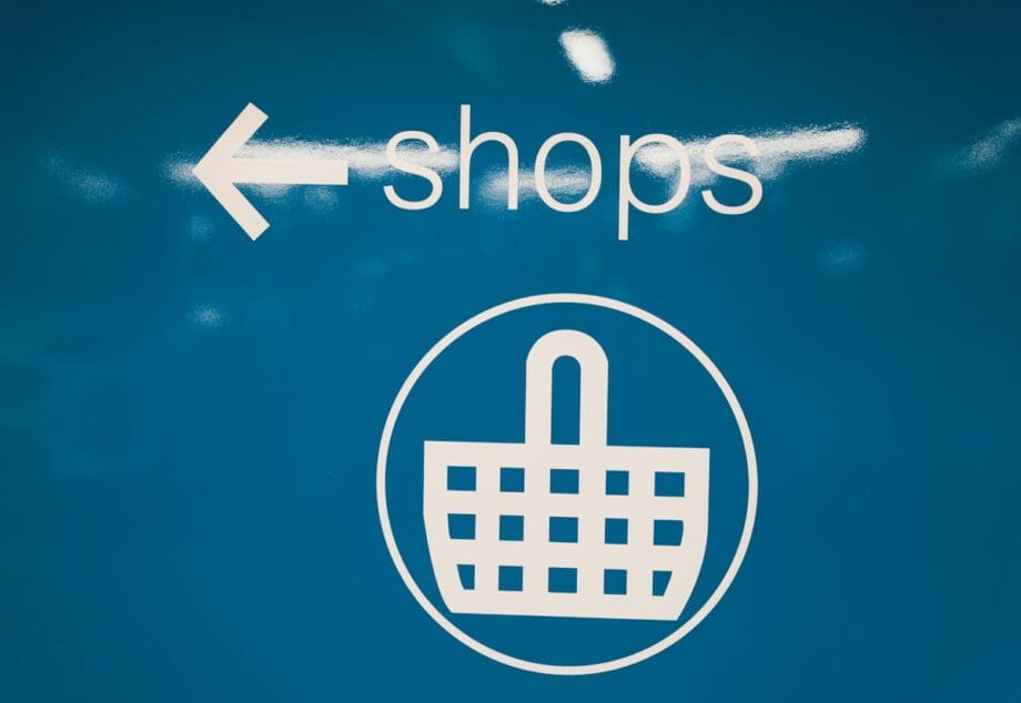 White text and icon on blue background showing an arrow pointing left, the word shops, and a shopping basket symbol.