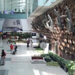 Travelers walk through an airport terminal with a large hand sculpture display and an advertisement for a Samsung Galaxy S24 Ultra.
