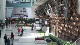 Travelers walk through an airport terminal with a large hand sculpture display and an advertisement for a Samsung Galaxy S24 Ultra.