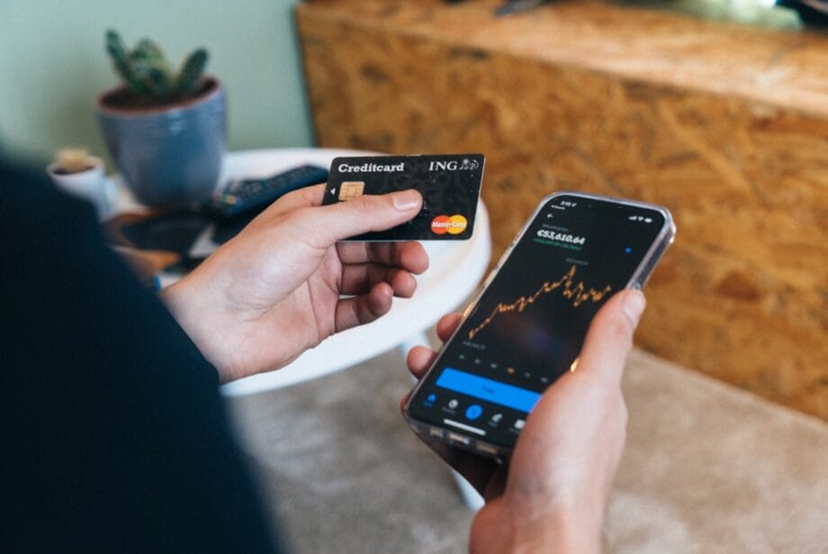 Person holding a credit card in one hand and a smartphone displaying a financial chart in the other hand indoors.