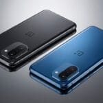 Two OnePlus smartphones, one black and one blue, are placed side by side on a reflective surface, showing their rear sides and cameras.
