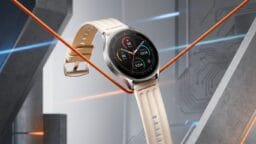 A beige smartwatch with a round display showing fitness metrics is suspended by orange wires in a modern, industrial setting.