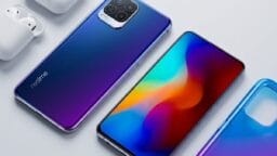 A Realme smartphone with a colorful display, its back shown alongside, next to white wireless earbuds and a case on a white surface.
