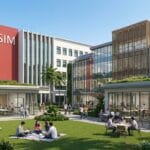 Modern campus courtyard with people sitting at tables and on grass, surrounded by contemporary SIM buildings under a clear sky.