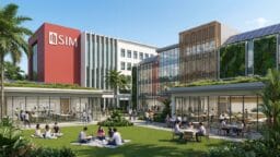 Modern campus courtyard with people sitting at tables and on grass, surrounded by contemporary SIM buildings under a clear sky.