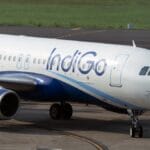 IndiGo aircraft taxiing on the runway at an airport, with a grassy area visible in the background.