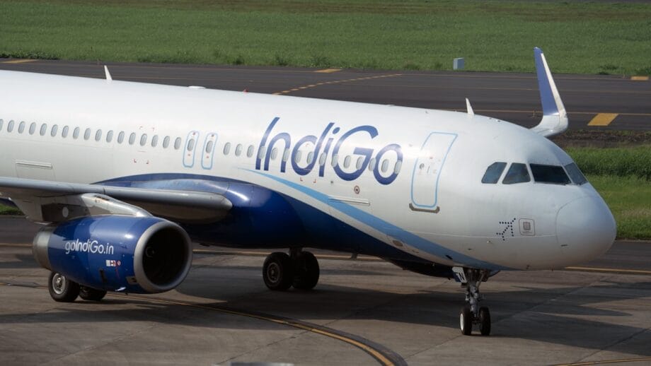 IndiGo aircraft taxiing on the runway at an airport, with a grassy area visible in the background.