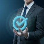 Businessperson in suit holding a glowing blue checkmark icon with a digital interface background.