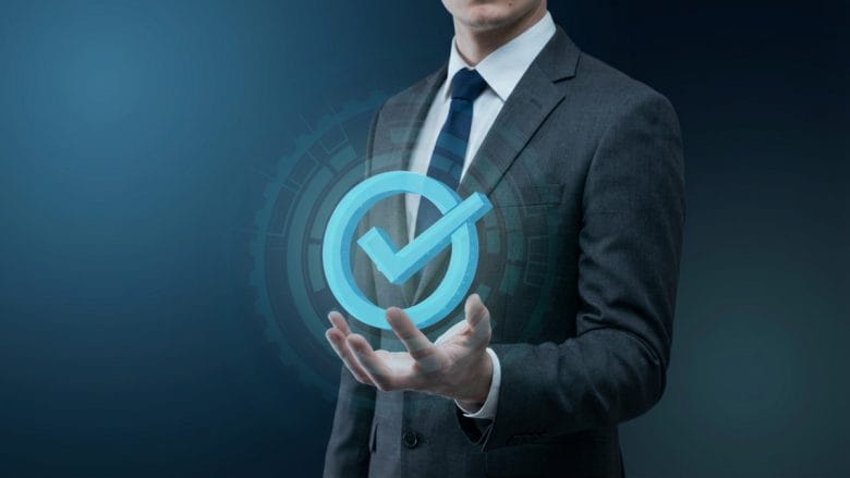 Businessperson in suit holding a glowing blue checkmark icon with a digital interface background.