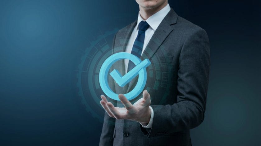 Businessperson in suit holding a glowing blue checkmark icon with a digital interface background.