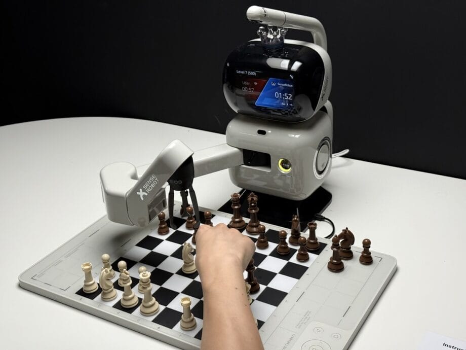 A person plays chess against a robotic arm with a digital screen showing game details on a black and white chessboard.