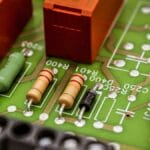 Close-up of an electronic circuit board showing resistors, a diode, capacitors, and visible circuit traces.