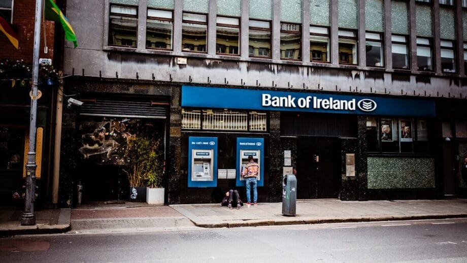 Person using an ATM outside a Bank of Ireland branch on a city street during daytime.