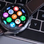 A smartwatch with a brown leather strap displaying colorful app icons rests on a laptop keyboard.