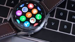 A smartwatch with a brown leather strap displaying colorful app icons rests on a laptop keyboard.