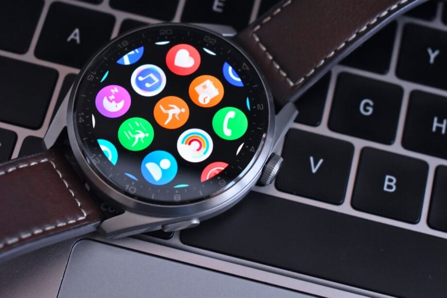 A smartwatch with a brown leather strap displaying colorful app icons rests on a laptop keyboard.