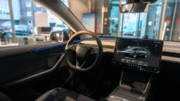 Modern electric car interior with a large central touchscreen display showing vehicle information, minimalistic dashboard, and steering wheel.