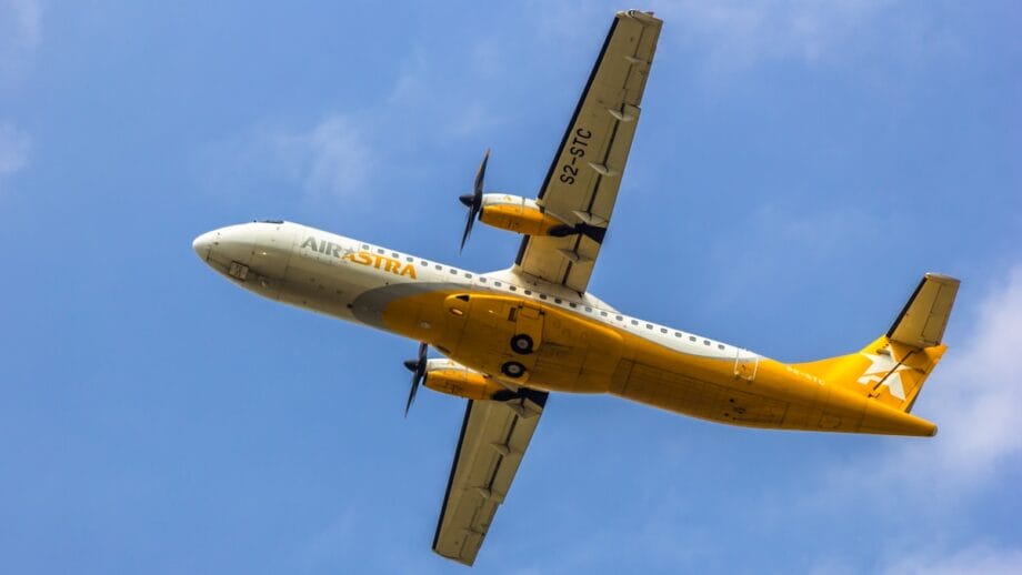 A yellow and white Air Astra propeller airplane flies overhead against a blue sky.