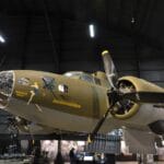 A World War II-era B-17 bomber aircraft displayed indoors at a museum, with exhibition panels visible below.