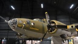 A World War II-era B-17 bomber aircraft displayed indoors at a museum, with exhibition panels visible below.