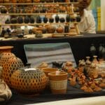Various handcrafted clay pottery items, vases, and figurines displayed on black cloth at a market stall.