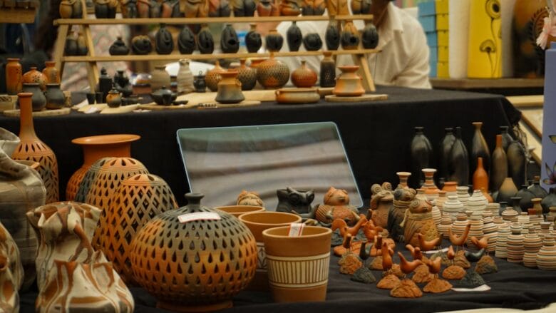 Various handcrafted clay pottery items, vases, and figurines displayed on black cloth at a market stall.