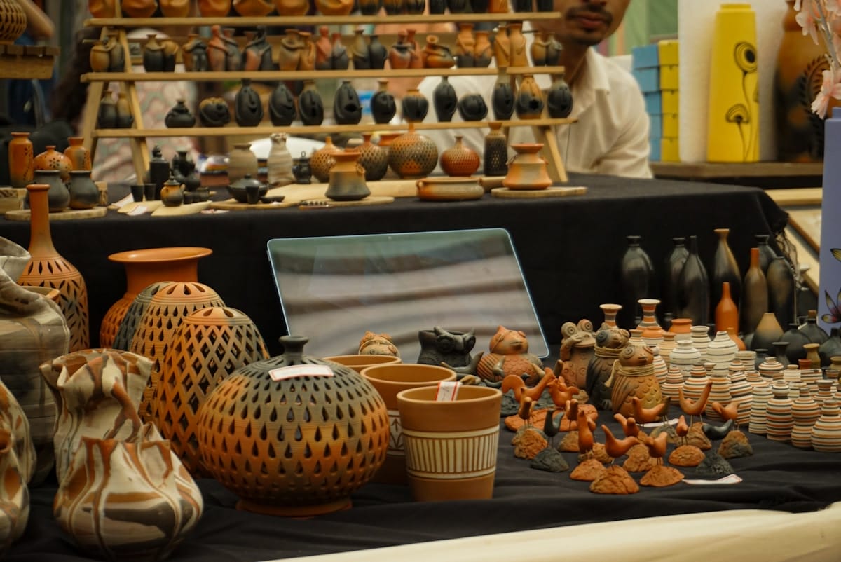 Various handcrafted clay pottery items, vases, and figurines displayed on black cloth at a market stall.