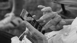An elderly person uses a smartphone, scrolling through photos with one hand while holding the phone with the other.