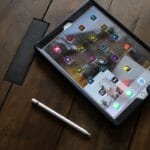 A tablet with various app icons on the screen and a stylus pen placed on a wooden surface.