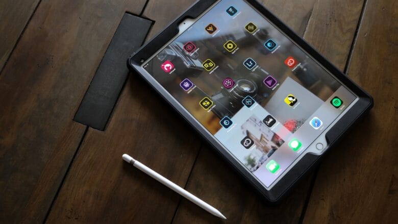 A tablet with various app icons on the screen and a stylus pen placed on a wooden surface.