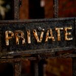 Close-up of a weathered metal sign with the word PRIVATE attached to a rusty gate.