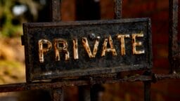 Close-up of a weathered metal sign with the word PRIVATE attached to a rusty gate.