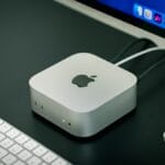 A silver Apple Mac Studio computer connected to a monitor, with a white Apple keyboard on a black desk.