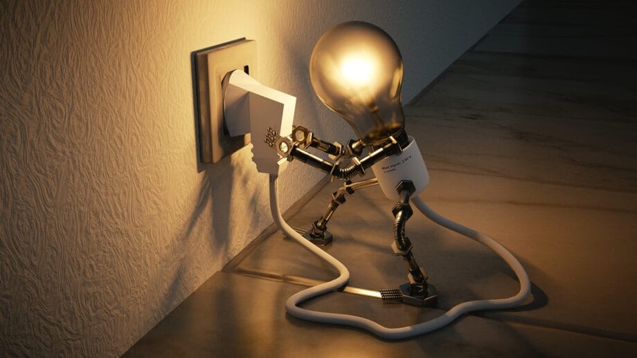 A lightbulb with mechanical arms and legs plugs an electrical cord into a wall socket, illuminating its own head.