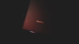 A OnePlus smartphones back cover with logo is partially illuminated against a dark background.