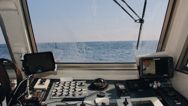 View from a boat cockpit showing navigation equipment, controls, and the ocean visible through the windshield.