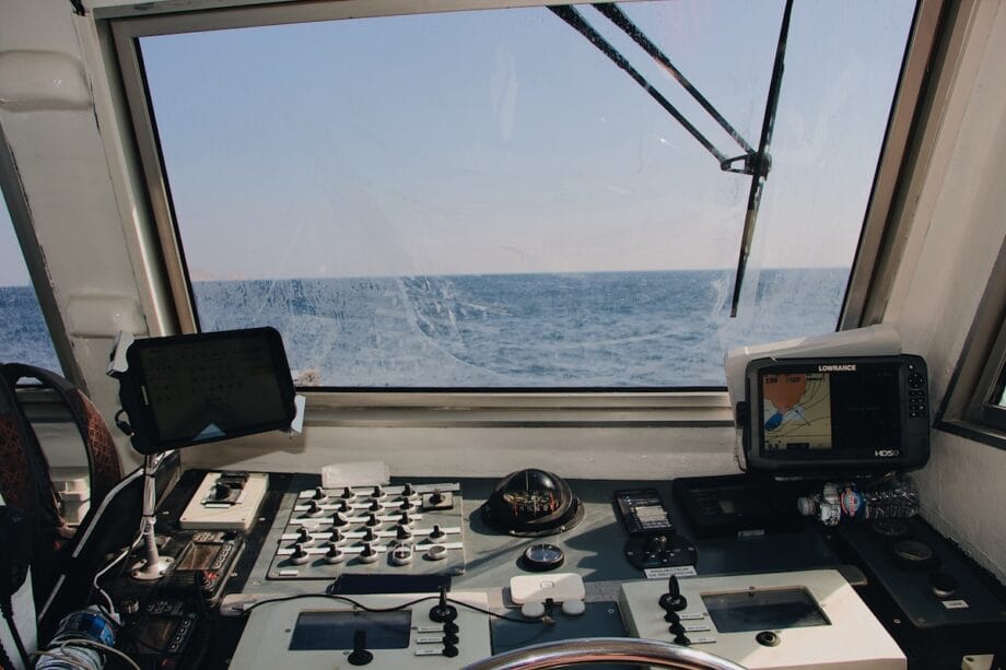 View from a boat cockpit showing navigation equipment, controls, and the ocean visible through the windshield.