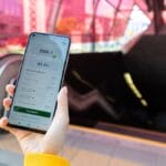 Person holding a smartphone displaying a loan app in front of an entrance to an underground metro station with red glass panels.