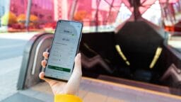 Person holding a smartphone displaying a loan app in front of an entrance to an underground metro station with red glass panels.