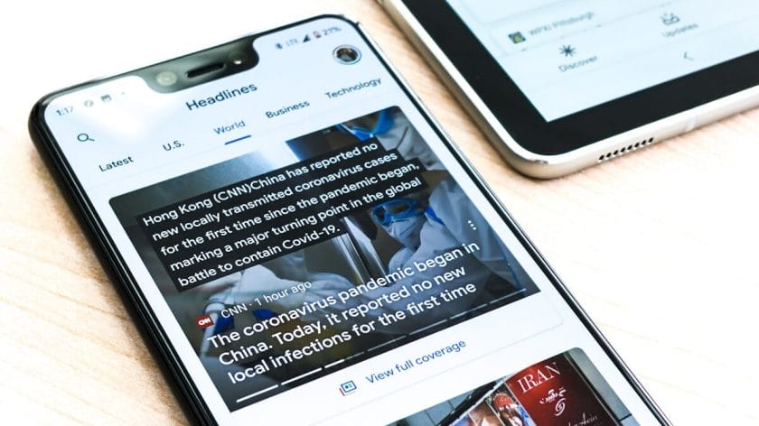 A smartphone displays a news article about the coronavirus pandemic, next to a tablet on a white surface.