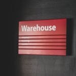 Red sign on a dark wall labeled Warehouse with smaller text for Shipping, Receiving, and Service.