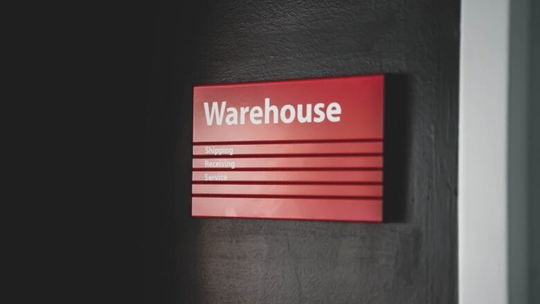 Red sign on a dark wall labeled Warehouse with smaller text for Shipping, Receiving, and Service.