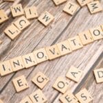 Scrabble tiles on a wooden surface spell out the word INNOVATION among scattered tiles with random letters.