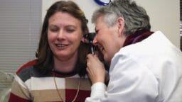 A healthcare professional examines a womans ear with an otoscope in a clinical setting.