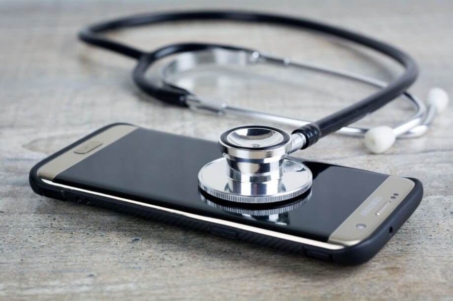 A stethoscope rests on top of a smartphone placed on a wooden surface.
